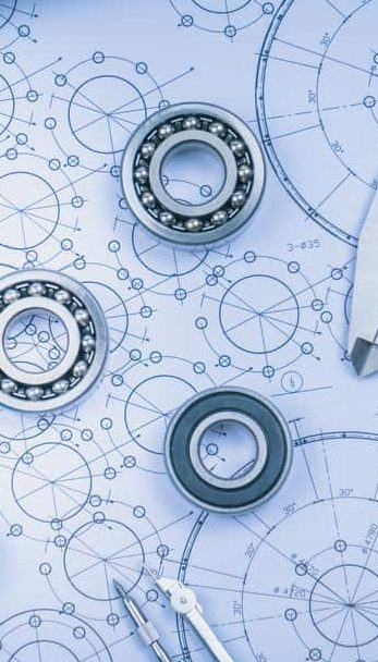Mechanical bearings placed on engineering blueprints with circular designs and measurement markings.